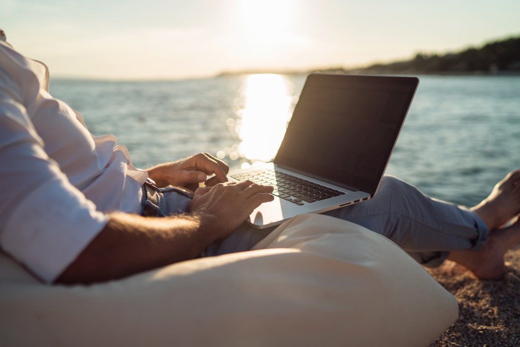A person working on a laptop while being on the beach